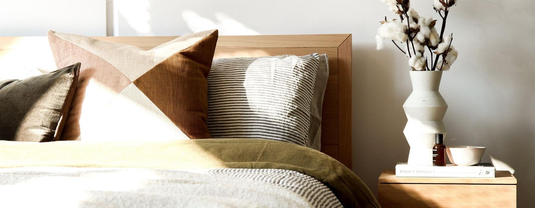 swath of sunlight shines across a well made bed and bedside table with a vase of cotton plants